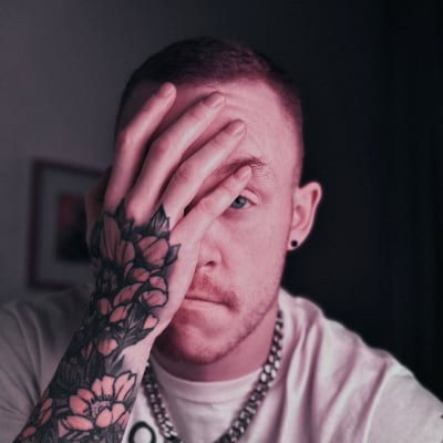A close up of a man with short hair, with one tattooed hand in front of his face